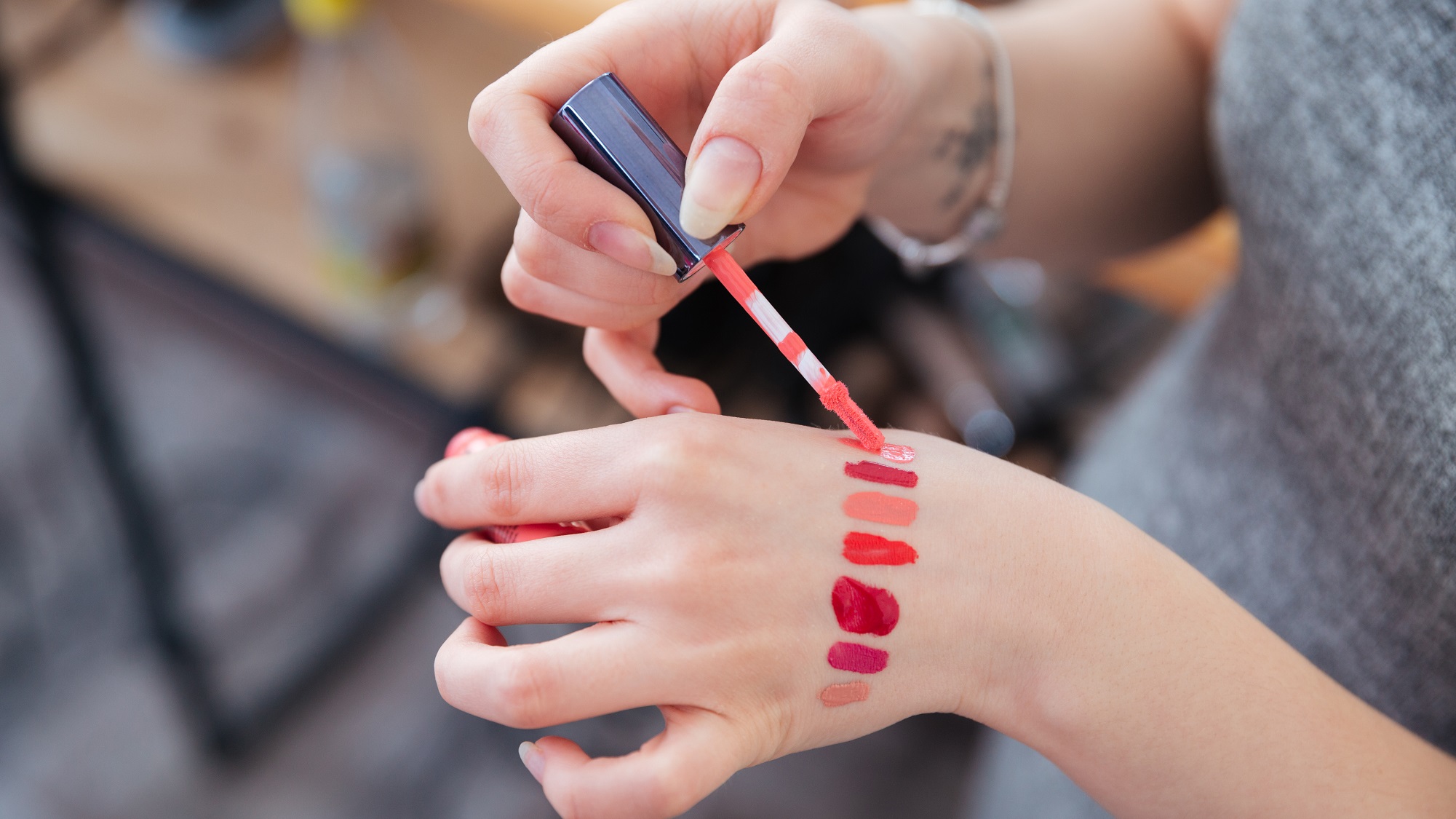 A person is applying lip glosses on her hand.