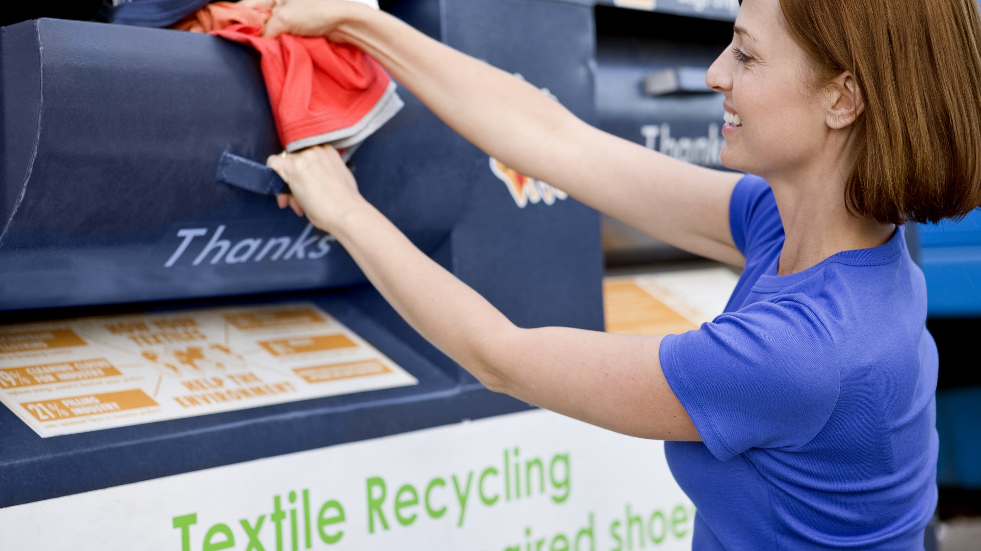 A woman placing the clothing into a textile recycling collection box.