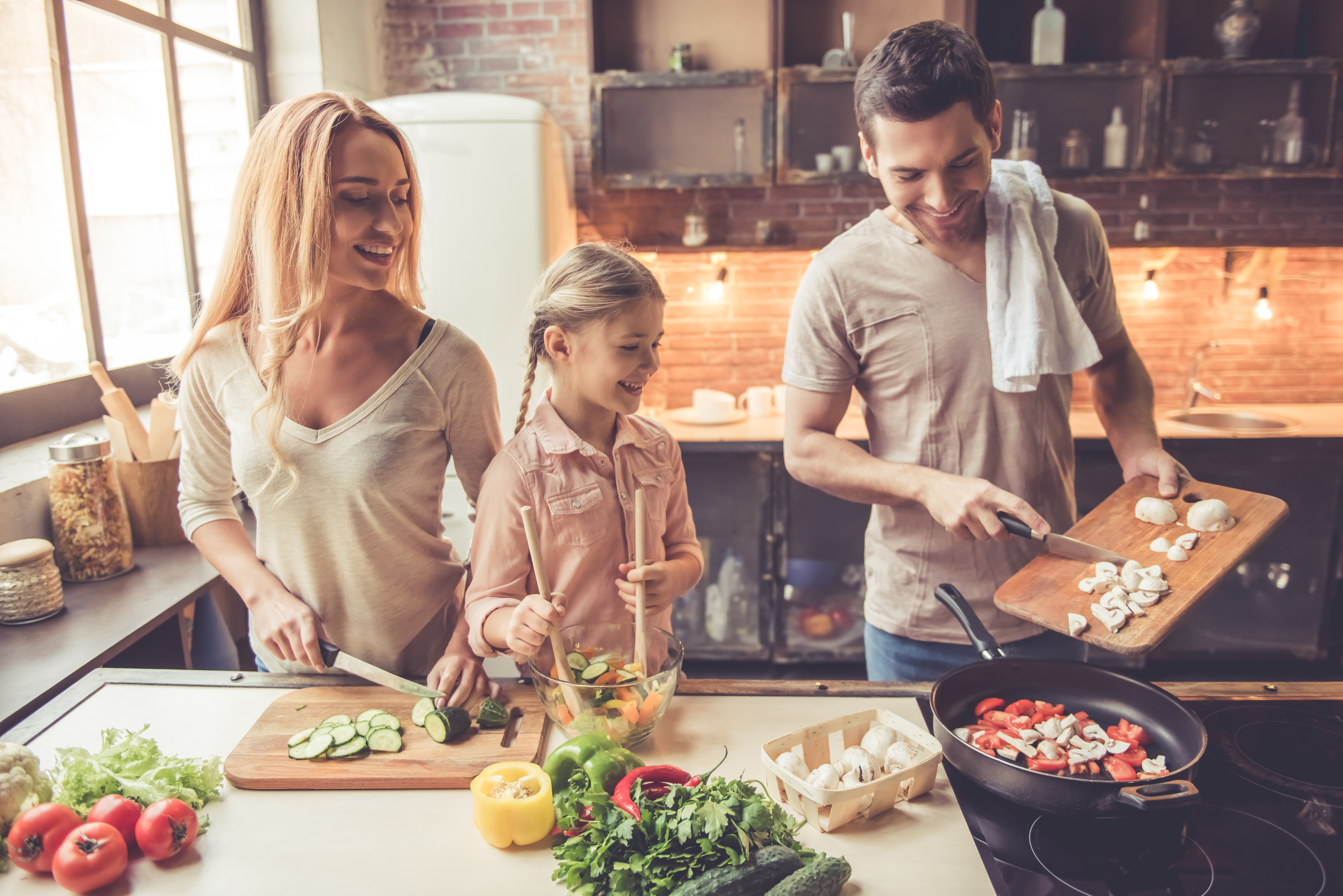 Cute little girl and her beautiful parents are smiling while cooking in kitchen at home