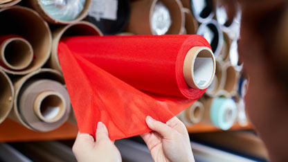 Person examining a roll of red fabric in a textile warehouse