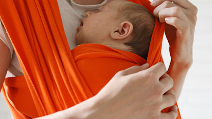 Newborn sleeping in an orange baby wrap, held close to the caregiver's chest