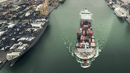 Cargo ship loaded with containers departs from a busy industrial port.