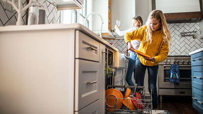 Two young girls load a dishwasher in a modern kitchen