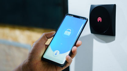 A person using a smartphone with a digital lock app near a wall-mounted access reader.