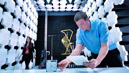 A technician in a blue shirt conducts a test in an anechoic chamber with a tablet