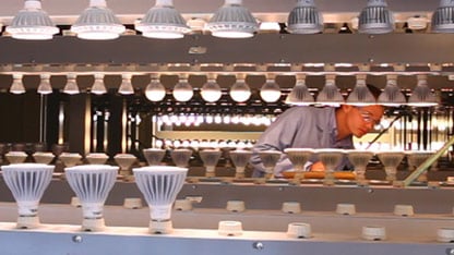  technician inspecting rows of LED and compact fluorescent light bulbs in a testing lab