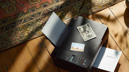 A printer on a wooden floor with photos and documents placed on and around it