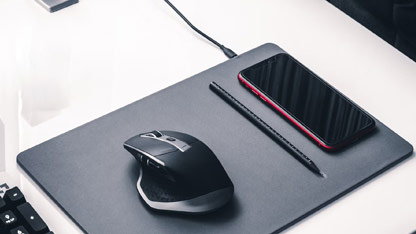 A wireless charging pad with a smartphone, mouse, and stylus placed on a minimalistic desk setup.