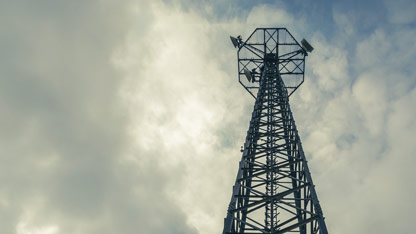 A tall radio or cell tower against a cloudy sky, used for broadcasting or telecommunications.