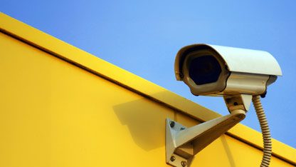 A security camera mounted on a bright yellow wall, angled to monitor the area