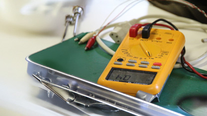 A yellow digital multimeter displaying a reading, placed on a green clipboard with test leads.