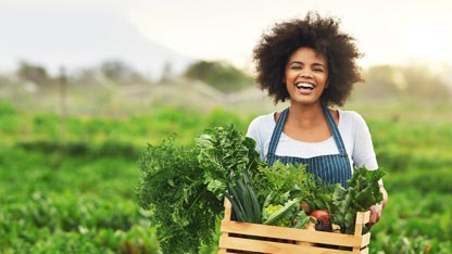 Smiling woman holding a box of fresh vegetables on a farm