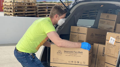 A man in a face mask and latex gloves loads a box of donated face masks into a card