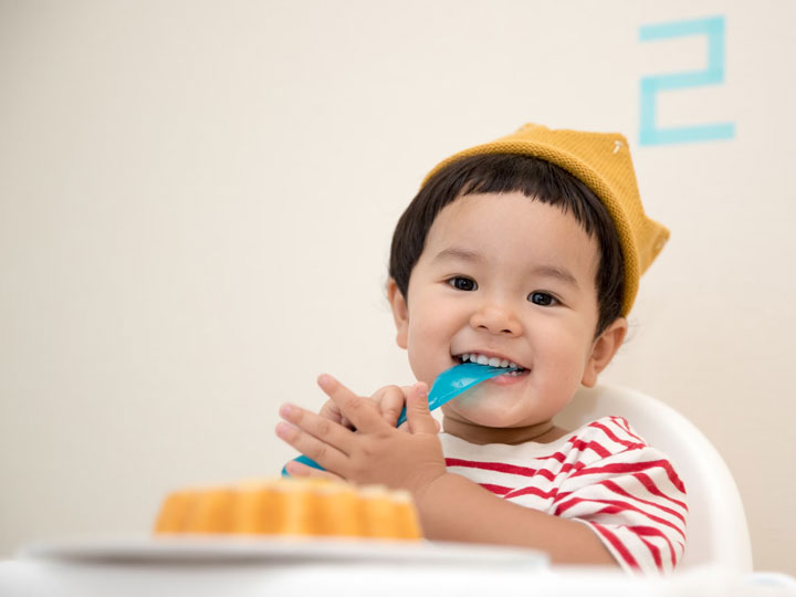 Young child in highchair with plastic fork in mouth